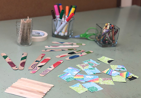 Materials to make a homemade puzzles on a table. Markers, paper, popsicle sticks and tape.