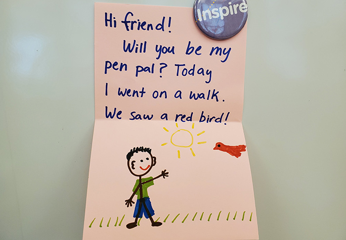 A handwritten note to a pen pal: Hi friend@ Will you be my pen pal? Today I went on a walk. We saw a red bird!