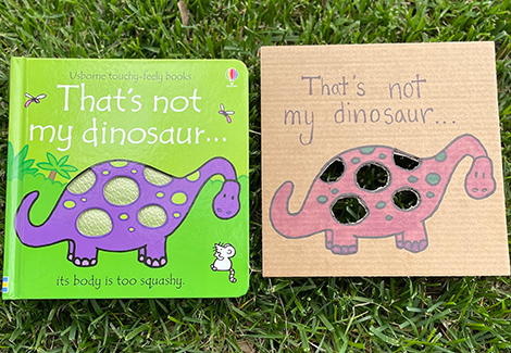 That's Not My Dinosaur Book and colored cardboard replica of the book sitting on a lawn