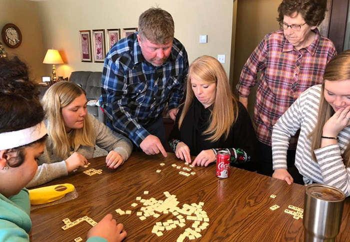 Teenagers and adults around a table playing a tile game called Bananagrams.