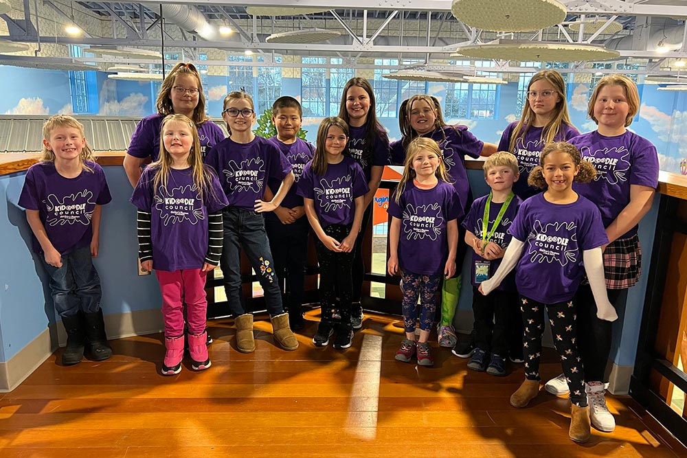 Group of 13 children in purple shirts smiling