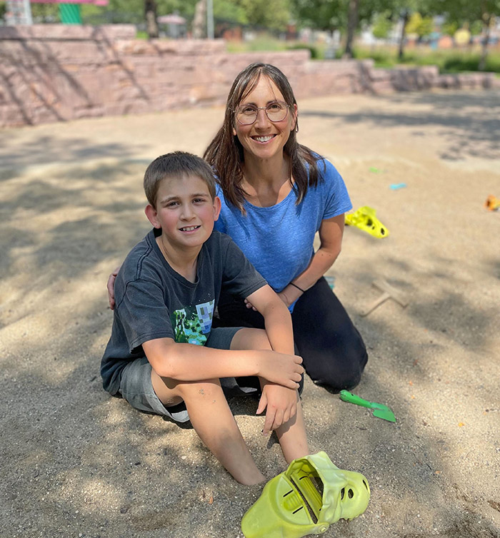 Woman and mom kneeling in a sand pit with dinosaur toys smiling at the camera