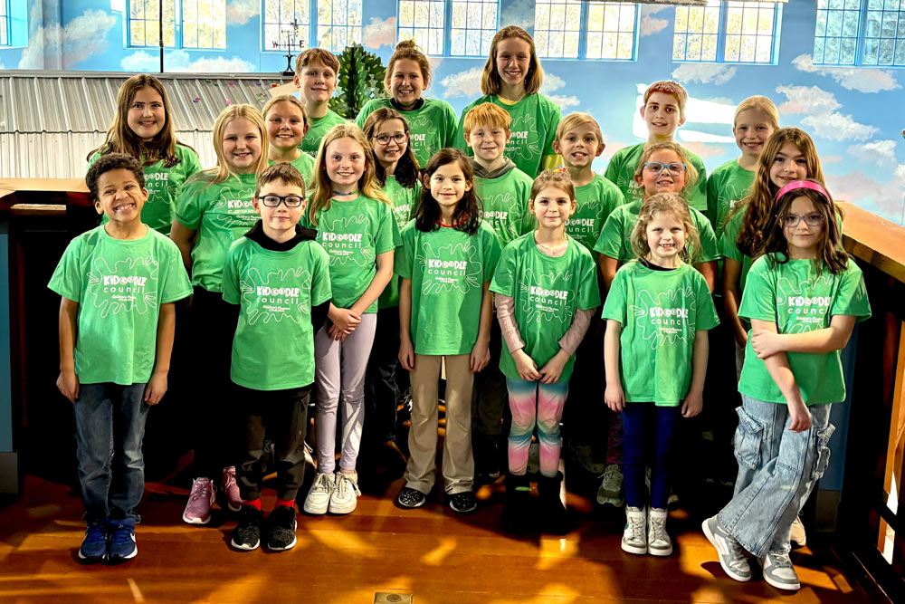 Group of children in green shirts smiling at the camera. This group is the Kidoodle Council Youth Advisory Board.