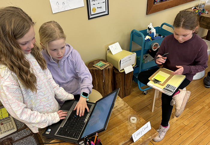 Three young students working at a desk in a maker studio. 
