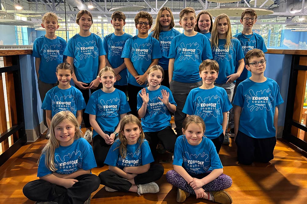 Group of children in turquoise shirts smiling at camera. They are ages 6-12.