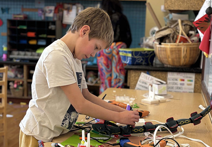Boy concentrates on creating an animal out of hot glue and various materials.