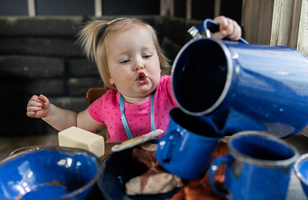 Little girl pouring pretend coffee out of a speckled camp coffee set.