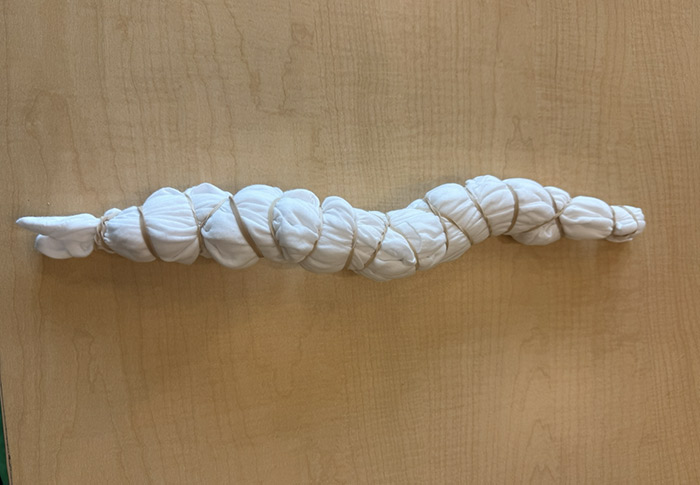 White tshirt that is all folded up in a long snake-like tube secured by multiple rubber bands. 