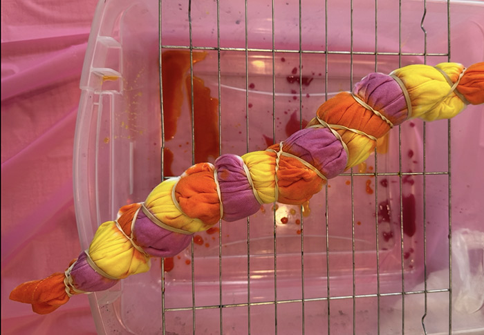 A tshirt is scrunched and rubberbanded and in the process of being tie-dyed over a plastic container. 